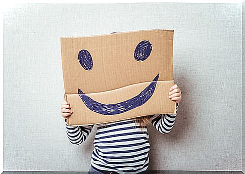 Child with a cardboard on which a happy face is drawn